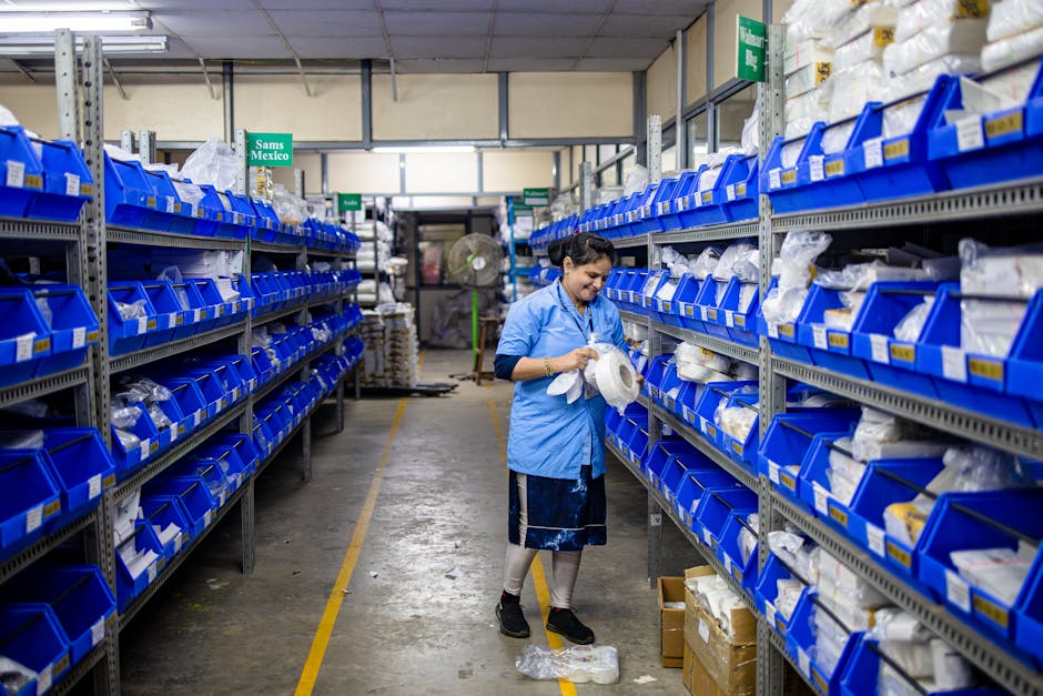 A woman organizing inventory in a warehouse aisle, surrounded by shelves and blue bins.