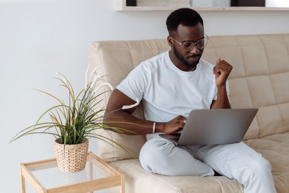 Confident young man sitting on a sofa using a laptop in a cozy home office environment.