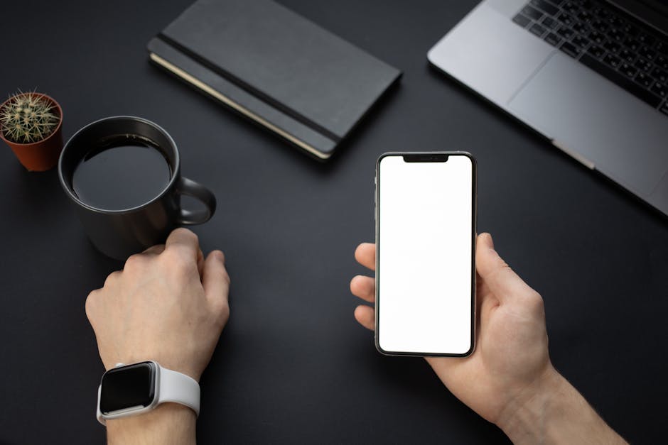 A minimalistic workspace setup featuring a smartphone, coffee mug, and smartwatch on a dark desk.