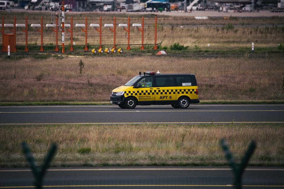 Yellow airport duty vehicle driving on runway with grassy background and clear blue day.