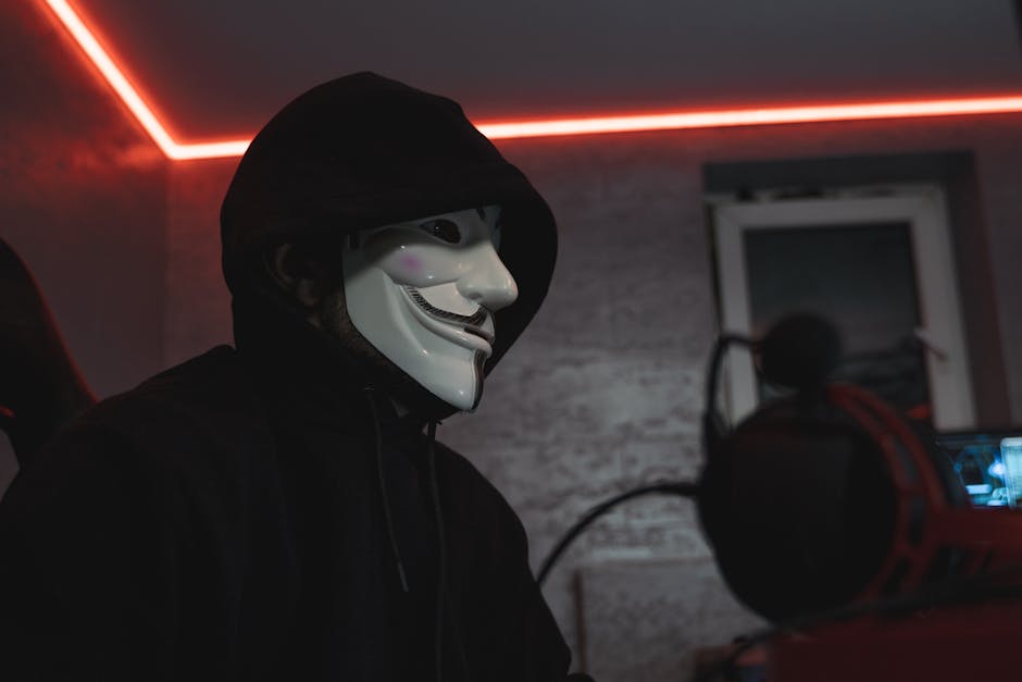 Person wearing a hacker mask in a dimly lit room, symbolizing cyber security.