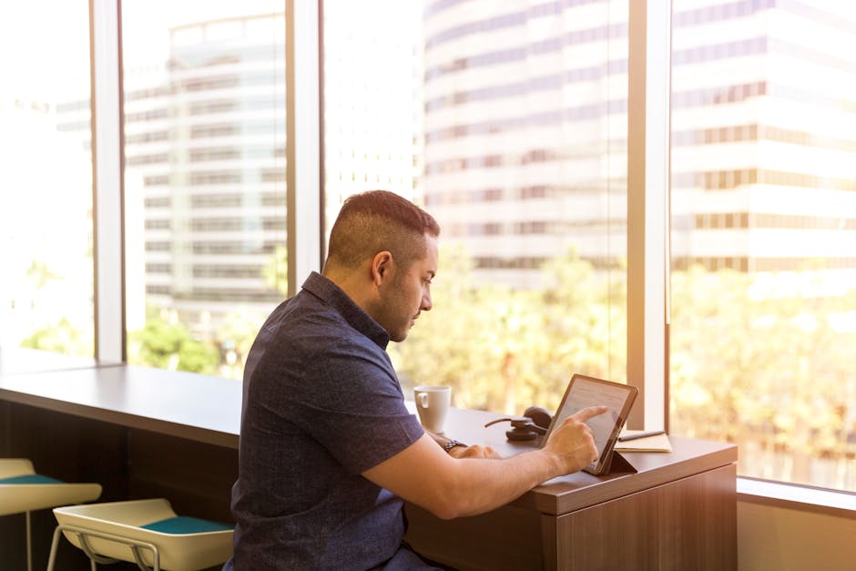 Side view of a man using a tablet in a bright office with city view.