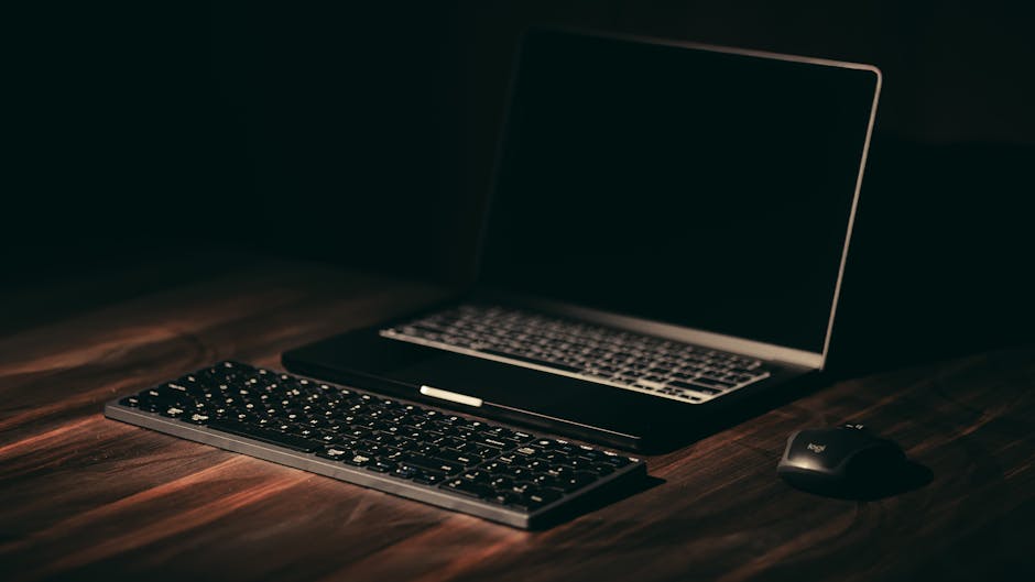 Minimalist dark-themed workspace with laptop and wireless keyboard.