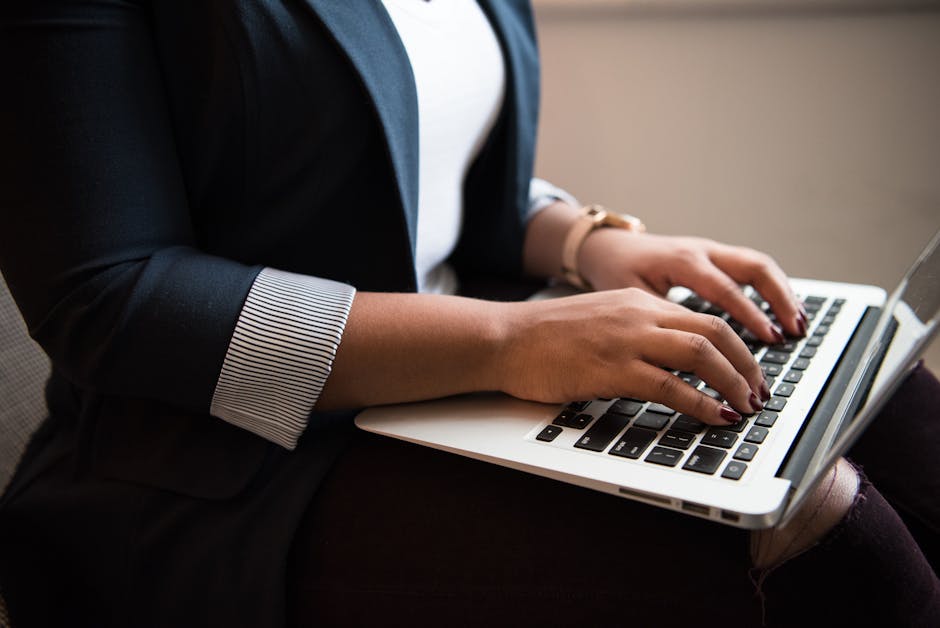 Woman in a blazer typing on a laptop in a well-lit room, focused on remote work.