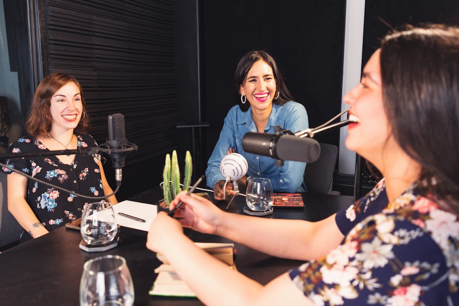 Three women sharing smiles and conversations during a podcast recording in a cozy studio setting.