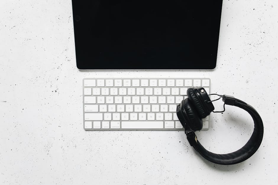Minimalist setup featuring a tablet, keyboard, and headphones on a white desk.
