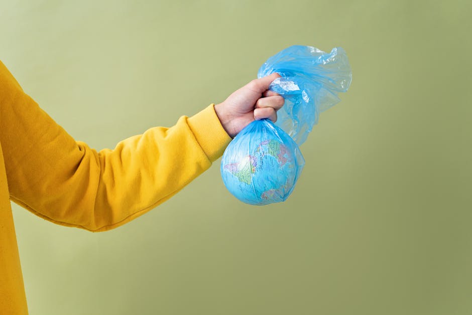 Hand holding Earth model in a plastic bag, highlighting pollution and environmental impact.
