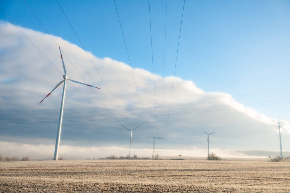 Wind turbines under a vast sky with cumulus clouds and power lines across a serene field.