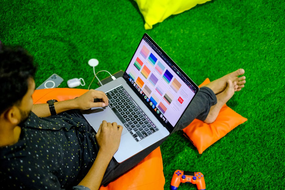 Man working on a laptop from home, seated on colorful cushions, showcasing digital designs.