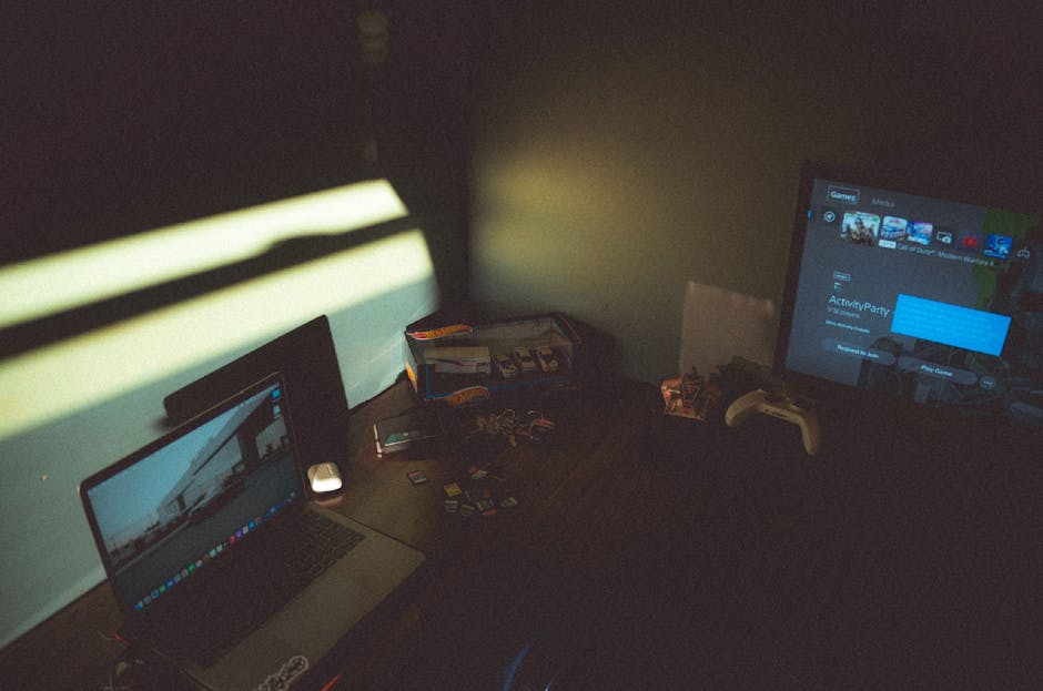 Dark room with a laptop and gaming console creating a moody tech atmosphere.