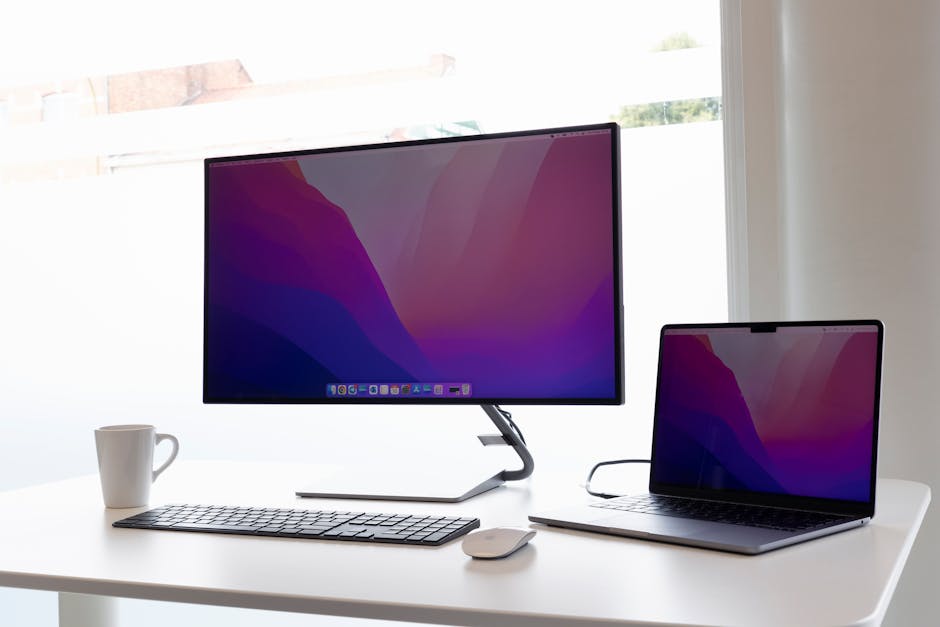 Sleek home office setup with a monitor, laptop, keyboard, and mouse on a minimalist desk.