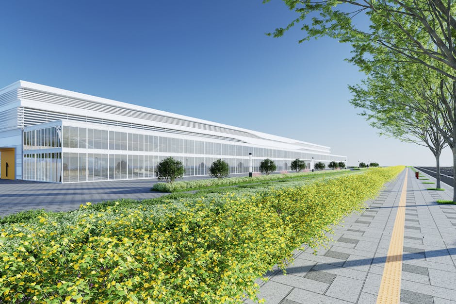 Contemporary industrial building exterior with a landscaped walkway, bright sky, and greenery.