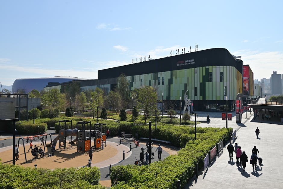 Busy outdoor shopping mall with a lively playground and lush greenery in daylight.