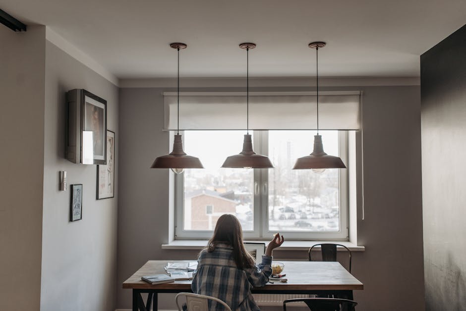 Person working from home in a modern dining room setup with laptop and snacks on the table.