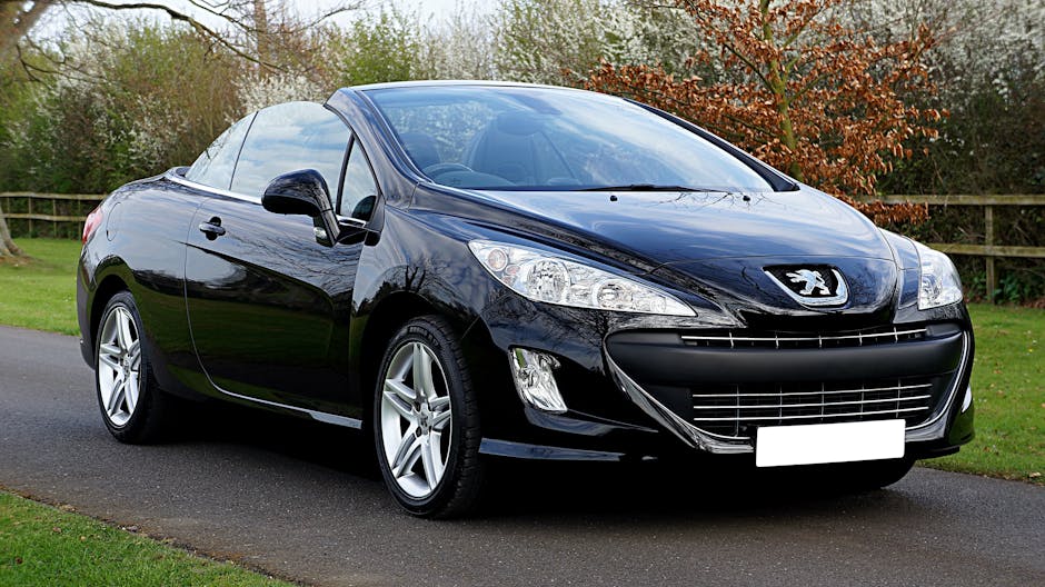 Black Peugeot 308cc convertible parked on a road in a serene outdoor setting in the UK.