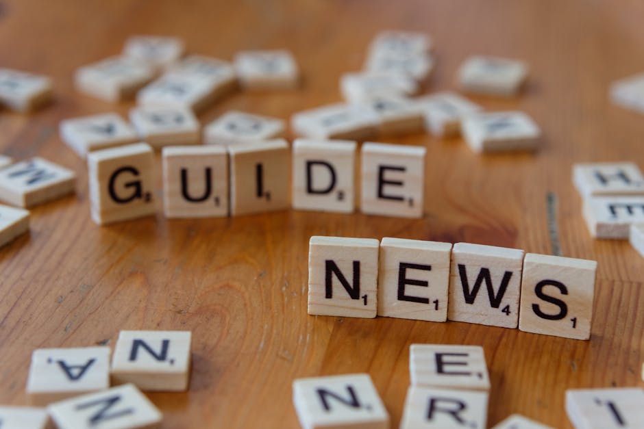 Close-up of Scrabble tiles spelling 'Guide' and 'News' on a wooden surface.