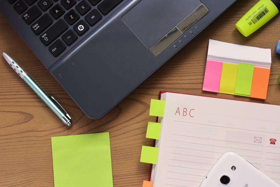 Top view of a workspace featuring a laptop, notebook, pen, and colorful stationery on a wooden desk.