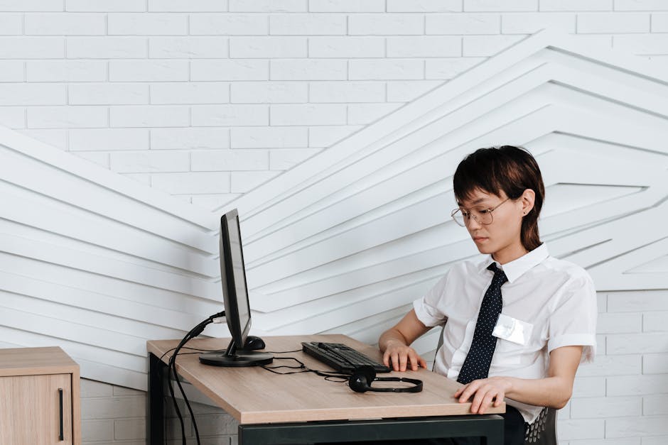 A young professional in an office setting, working on a desktop computer with a headset.