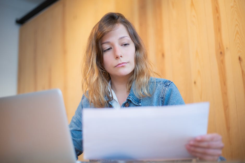 Businesswoman in a denim jacket analyzing documents at a wooden table in a cozy workspace.