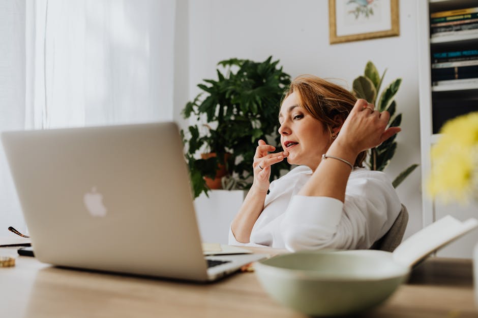 Professional woman working from home office using a laptop, with greenery in the background.