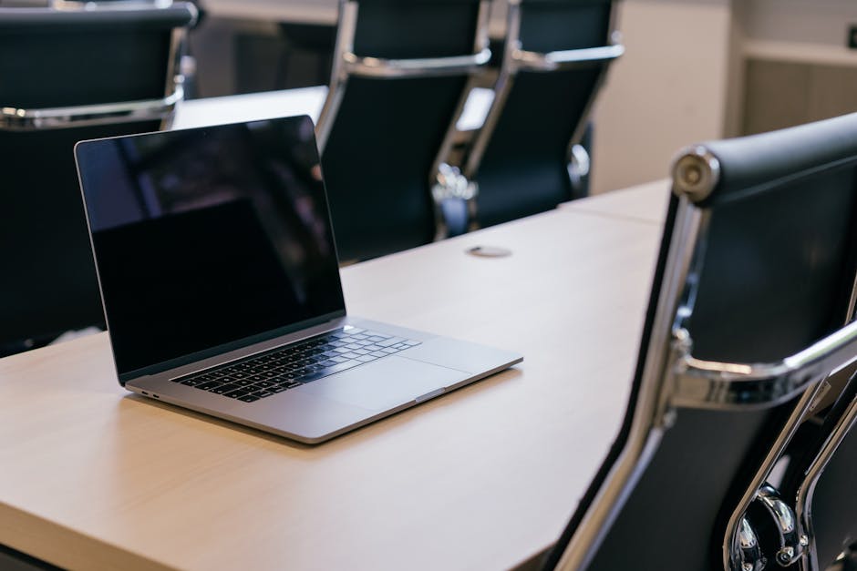 Open laptop on a wooden conference table with stylish black chairs in a modern office setting.