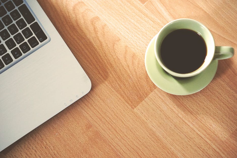 A coffee cup and laptop on a wooden desk, creating a cozy workspace vibe.