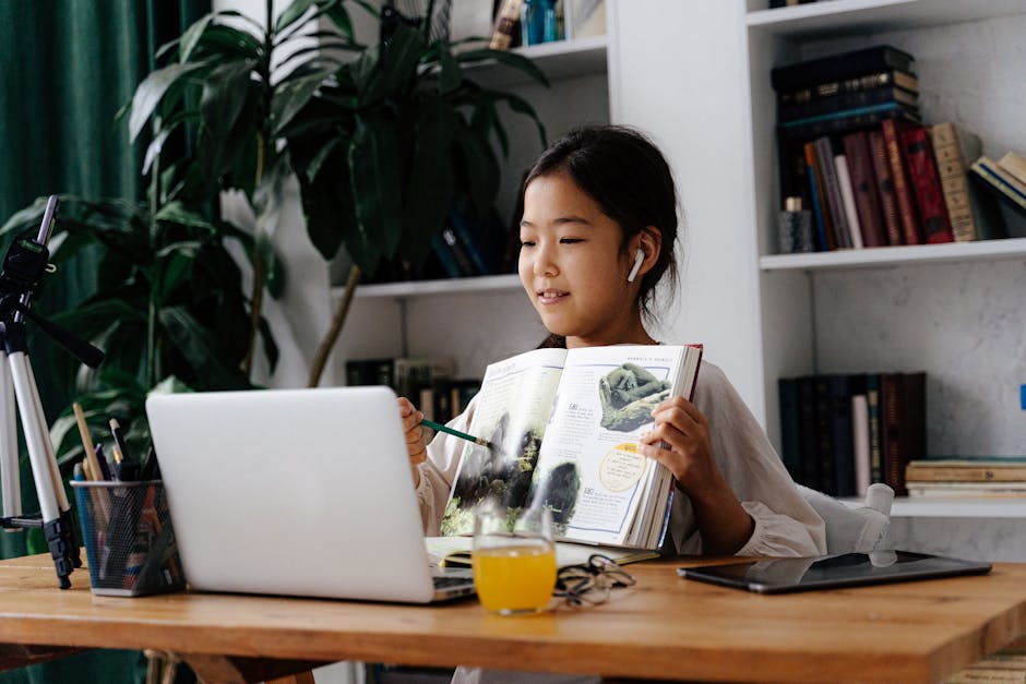 Asian child studying at home with a book and laptop, engaged in video calling.