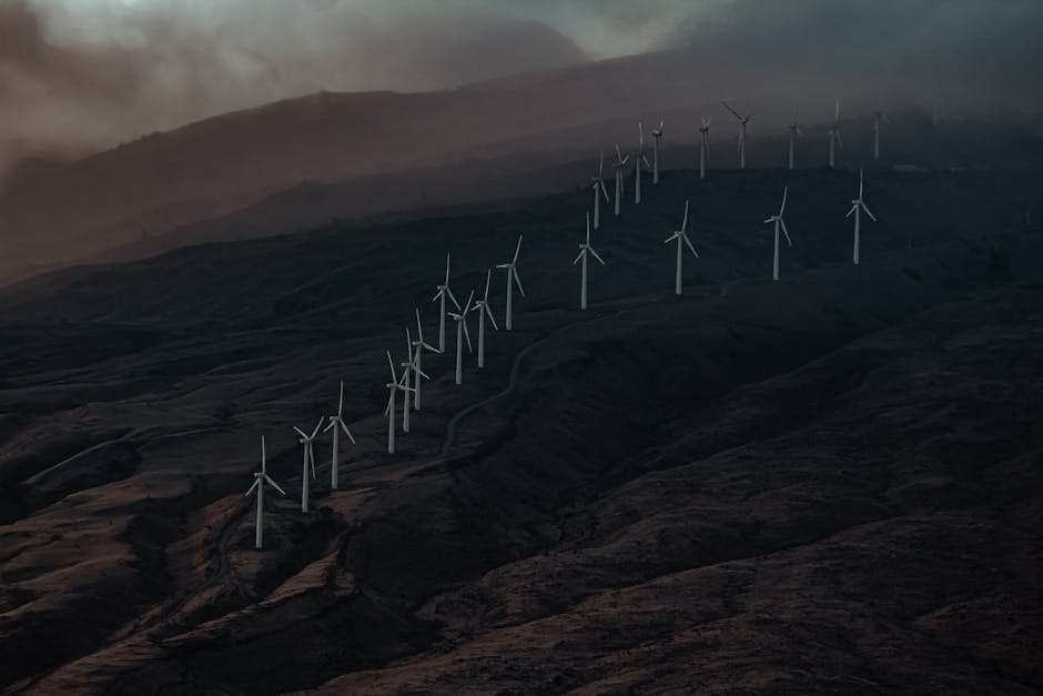 Aerial view of a wind farm with turbines on a misty mountainside during twilight.