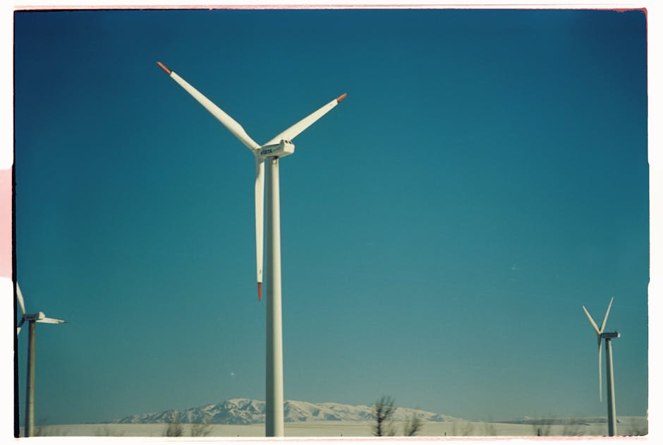 Wind turbines generating power under a clear blue sky with mountains in the background.