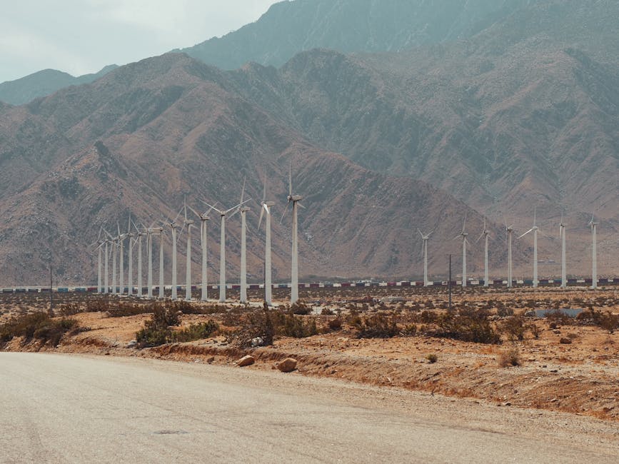 Line of wind turbines in a desert with mountains, showcasing renewable energy in nature.