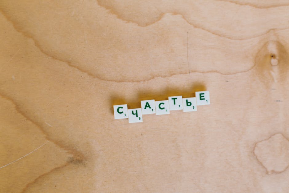 Scrabble tiles spelling 'Happiness' in Cyrillic on a light wooden surface.