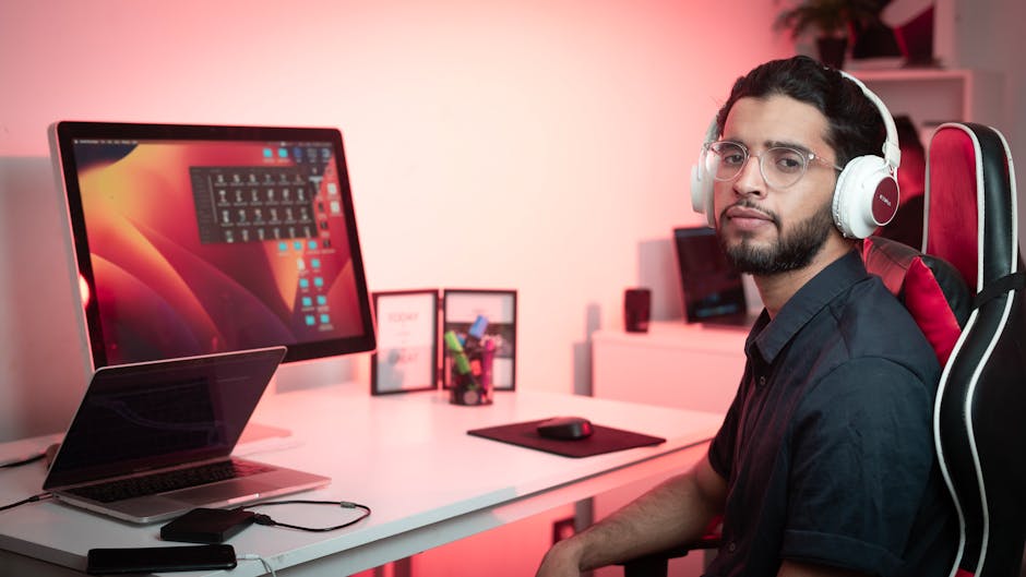 Young man with headphones working at a desk with dual screens in a modern office setting.