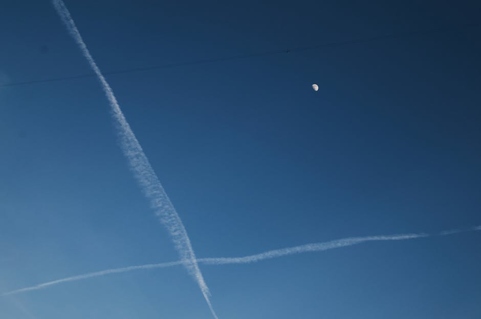 Clear blue sky with contrails crossing under the moon, captured over Moscow.