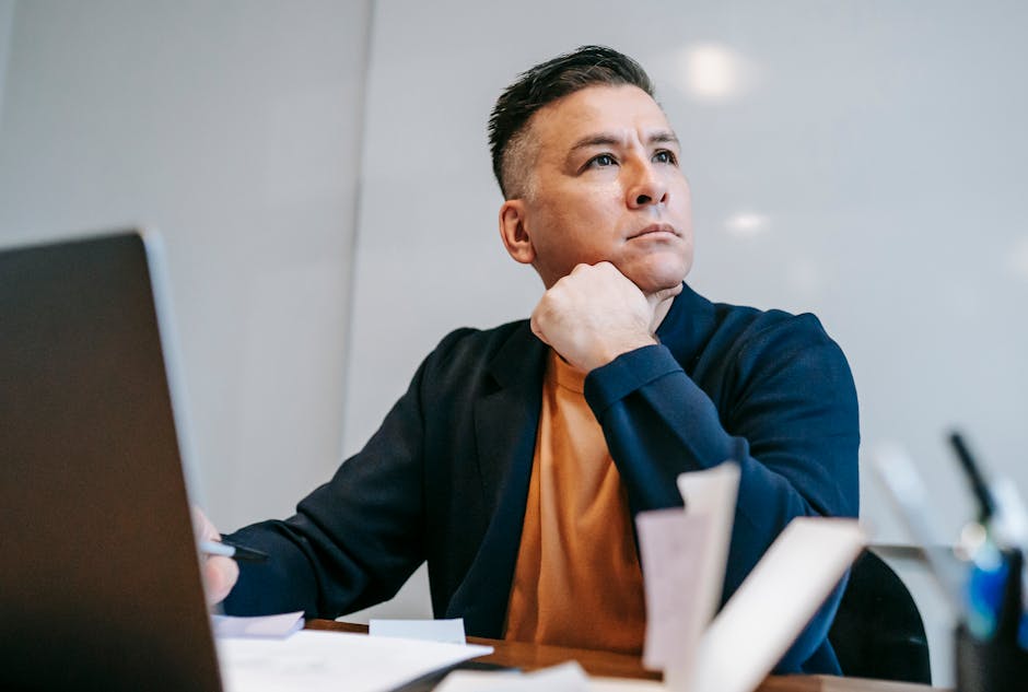 A focused man working remotely at a home office with a laptop and documents around.